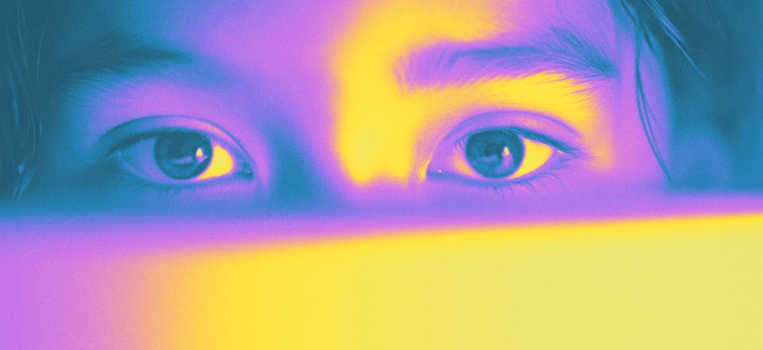 A close-up of a young boy's eyes lit by a colorful screen.