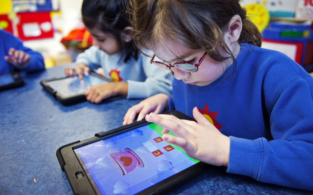 Two young students using tablet computers in a classroom.